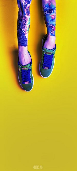 Tattooed legs wearing green Puma sneakers with blue laces