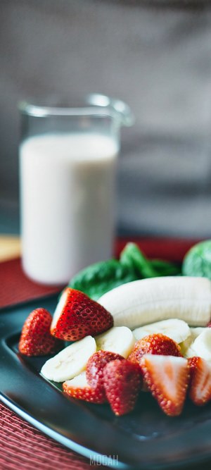 Strawberries, banana slices, and spinach with a jug of milk