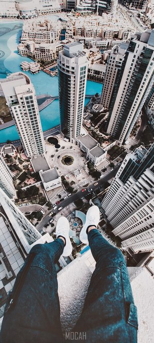 Person sitting on the edge of a skyscraper overlooking a city