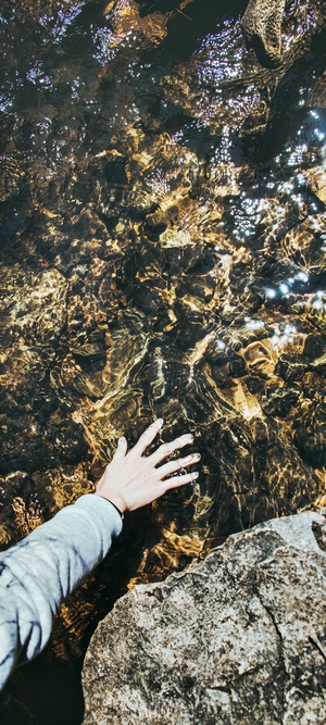 Hand touching clear water over rocks