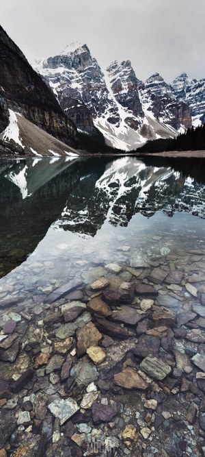 Snow-capped mountains reflected in a clear lake with rocky bottom