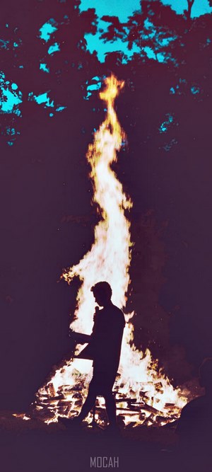 Silhouette of a person by a large bonfire