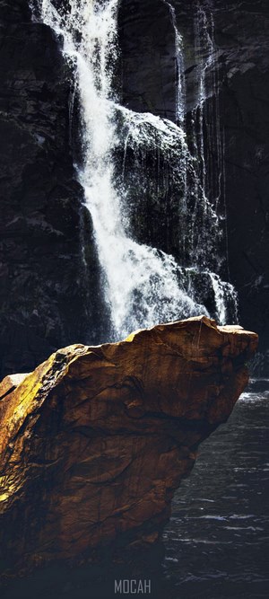Waterfall cascading over dark rocks with a large rock in the foreground