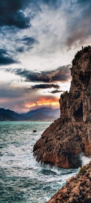 Person on cliff overlooking ocean and mountains at sunset