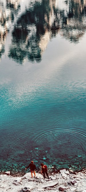 Two people by a lake with mountain reflection