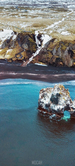 Coastal rock arch with waterfall and black sand beach