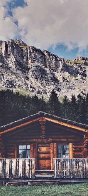 Log cabin in front of a rocky mountain and forest