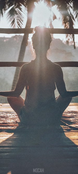 Woman meditating outdoors with palm trees and sun flare