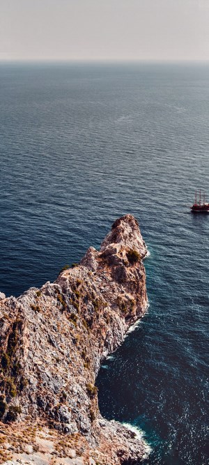 Rocky cliff overlooking the deep blue sea with a ship