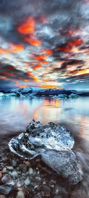 Iceberg on rocky shore with colorful sunset sky