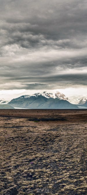 Snow-capped mountains over a barren field under a cloudy sky