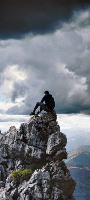 Man sitting on a rocky mountain peak under stormy clouds