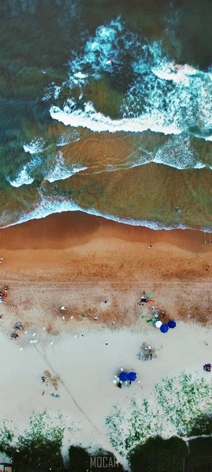 Aerial view of waves on a beach with people and umbrellas