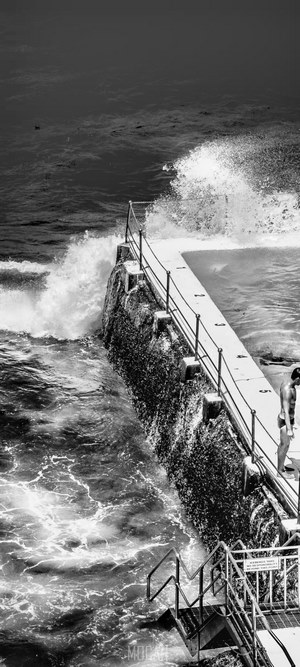 Man standing by ocean pool with waves crashing