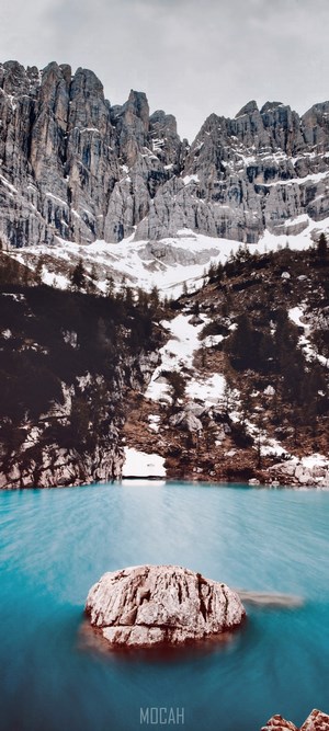 Turquoise glacial lake with a large rock and mountain range