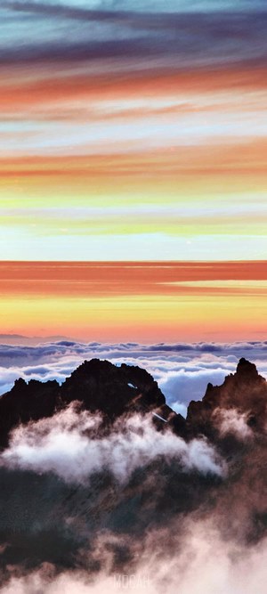 Jagged mountain peaks emerge from clouds at sunset