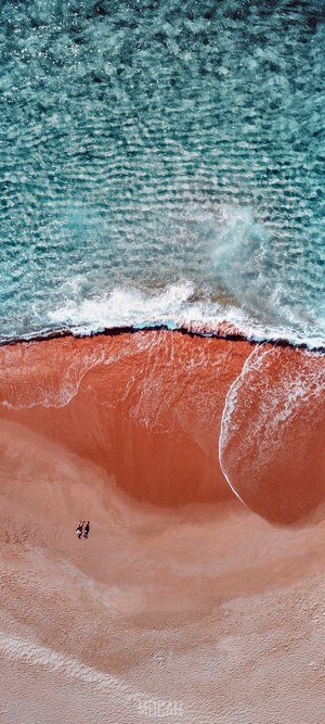 Two people walking on a beach with ocean waves