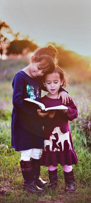 Two young girls reading a book outdoors at sunset