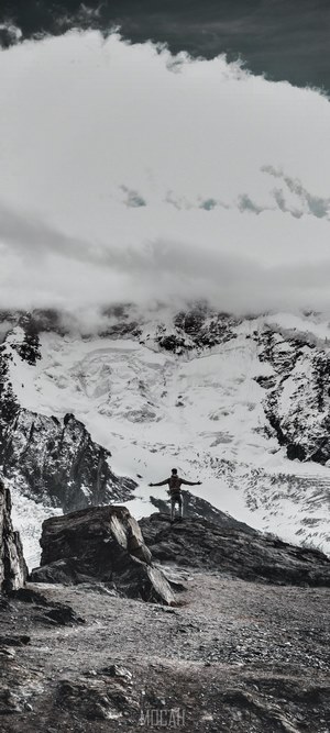 Man on mountain peak with snowy mountains and clouds