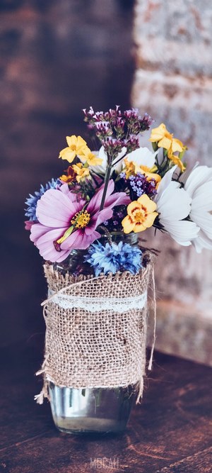 Bouquet of various flowers in a burlap-wrapped glass vase