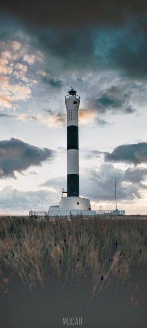 Black and white lighthouse on a grassy field under cloudy sky