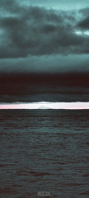 Mountain island on the horizon over the sea under dark clouds