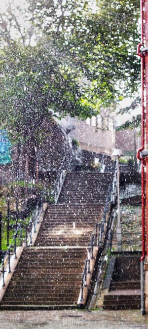 Rain falling on outdoor stone staircase with trees and brick building