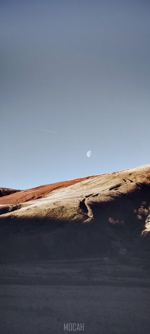 Moon over a sunlit hillside