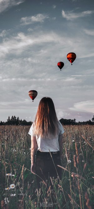 Girl in field watching hot air balloons