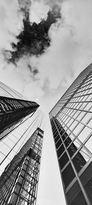 Monochrome low angle shot of glass skyscrapers under cloudy sky