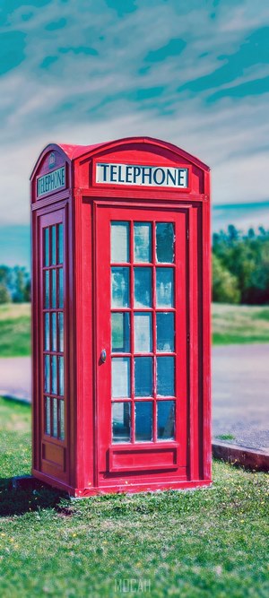 Red telephone booth on grass under blue sky