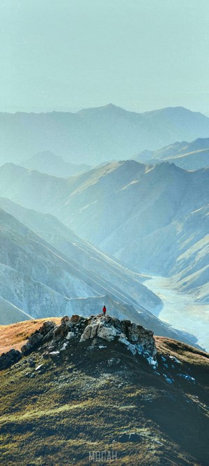 Person in red standing on a rocky mountain peak overlooking a valley