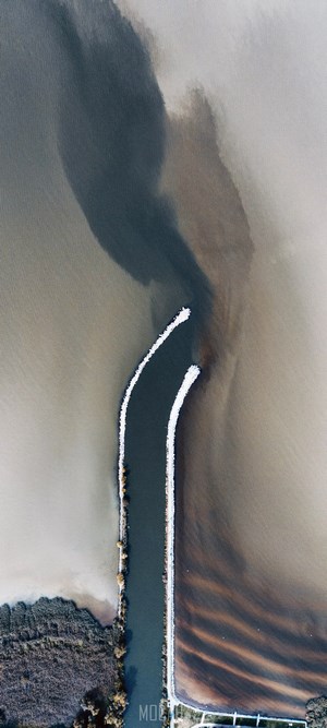 Aerial view of water meeting land with dark sediment plumes
