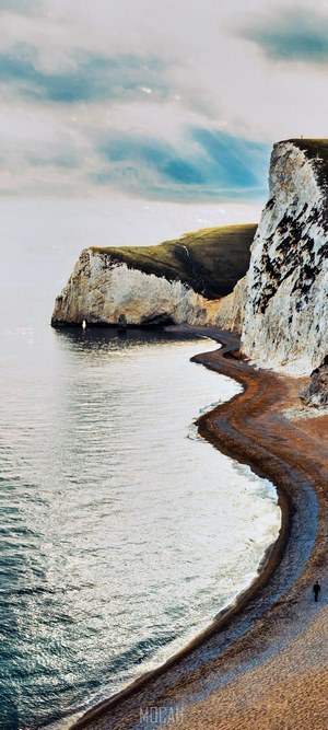 Man walking on a pebble beach near white cliffs