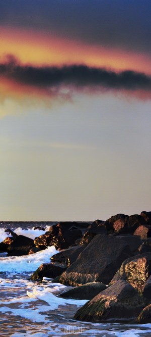 Sunset over the ocean with rocks and waves