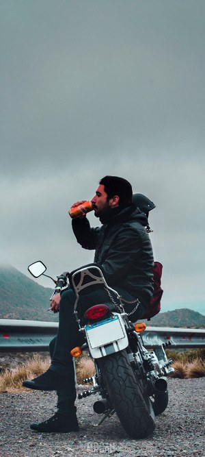 Man in jacket drinking from can on motorcycle