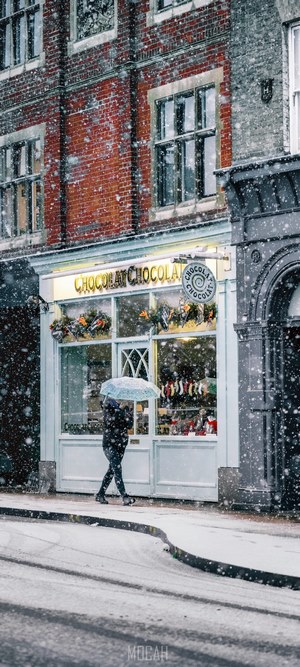 Person with umbrella walking past Chocolat shop in snow