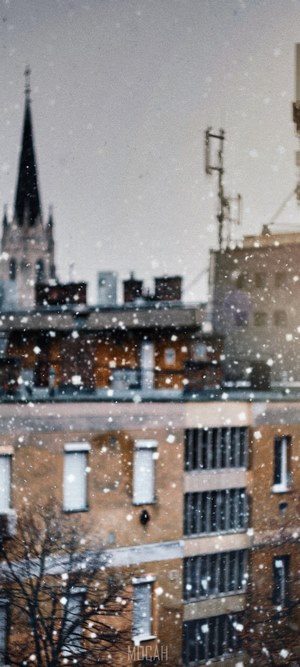 Snowing over city buildings with a church spire
