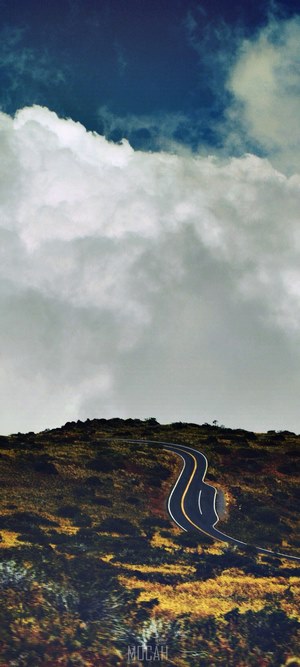 Road winding through a grassy hill under a cloudy sky