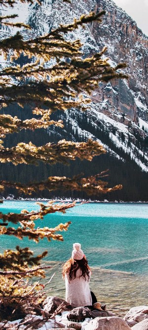 Woman sitting by Lake Louise with snowy mountains