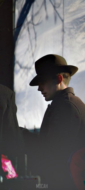 Man in hat and coat with tree shadows
