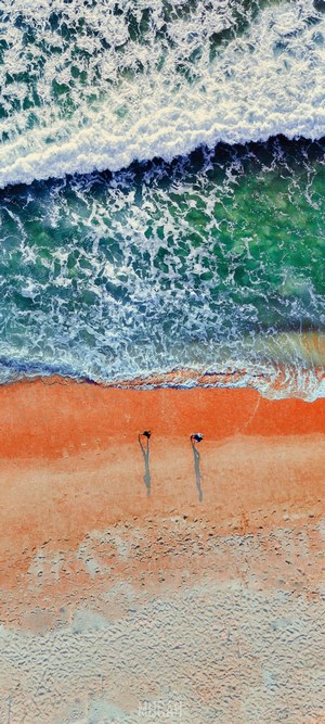 Two people walking on a beach with ocean waves