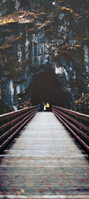 People on a wooden bridge leading to a dark tunnel in a rocky mountain