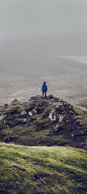 Person standing on a rocky hill overlooking a misty landscape