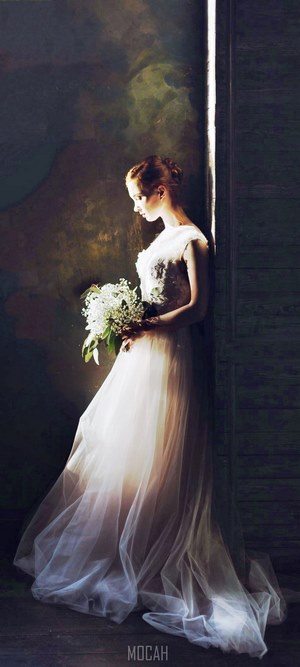 Bride in wedding gown with floral bouquet in shadows