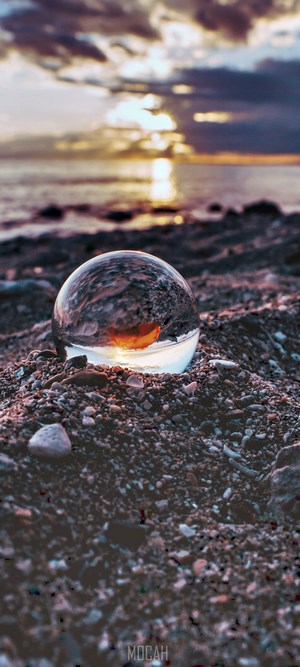 Sunset Reflection in Glass Sphere on Rocky Shore