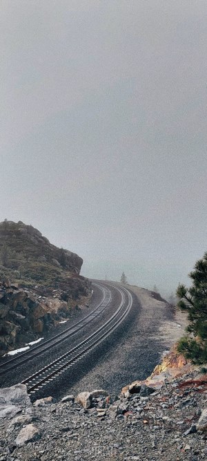 Railroad tracks curve through a foggy mountain landscape