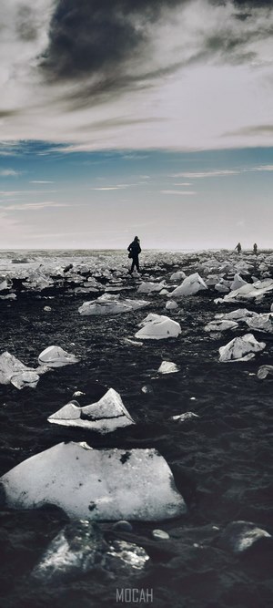 People walking on a black sand beach with ice chunks