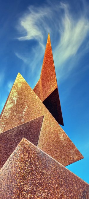 Rusty metal sculpture against a blue sky with wispy clouds