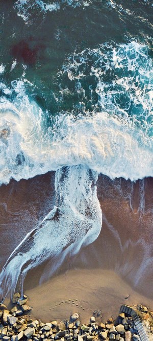 Aerial view of waves crashing on a sandy beach with rocks